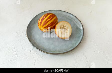 Vietnamese melon on a gray plate on a white background. Miniature fruit with pineapple flavor. Copy space. Stock Photo