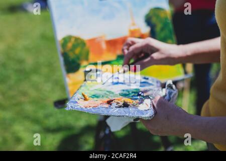 Process of plein air painting, group class of adult talented students in the park with paints easels, and canvases during lesson of watercolour painti Stock Photo
