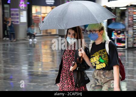 Belgrade, Serbia - August 5, 2020: Two young women wearing face surgical masks and colorful street style grunge fashion outfit walking under umbrellas Stock Photo