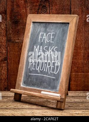 face masks required - white chalk handwriting on a blackboard, coronavirus covid-19 pandemic concept Stock Photo