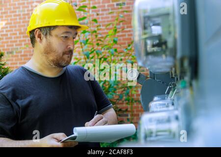 Close up of electrical engineer in yellow helmet technician writing on clipboard in front fuse box Stock Photo