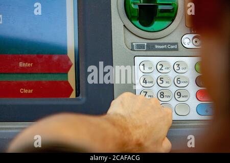 Man at a bank drive-thru ATM machine presses on keypad next to screen to withdrawal cash Stock Photo