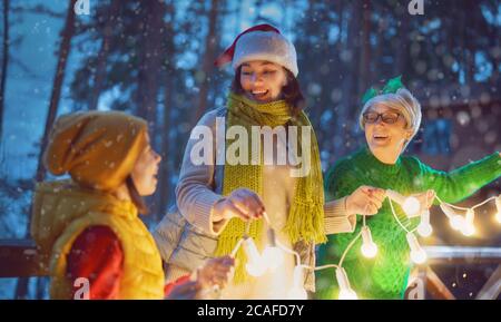 Merry Christmas and Happy Holidays! Cheerful mom, granny and cute girl decorating home. Parents and little child having fun outdoors. Loving family wi
