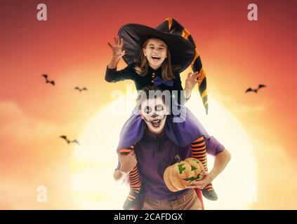 Happy family celebrating for Halloween! Young dad and his kid in carnival costumes on sunset background. Stock Photo