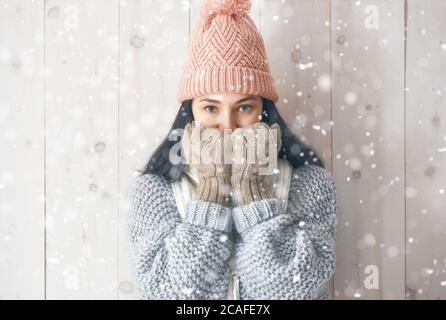 Winter portrait of happy young woman wearing knitted hat, scarf and sweater. Girl having fun on white wooden background. Fashion concept. Stock Photo