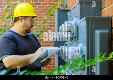 Electrician examining in yellow helmet technician writing reading of meter on clipboard Stock Photo
