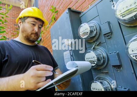 Electrical engineer on during checking in yellow helmet technician examining of doing meter reading on clipboard Stock Photo