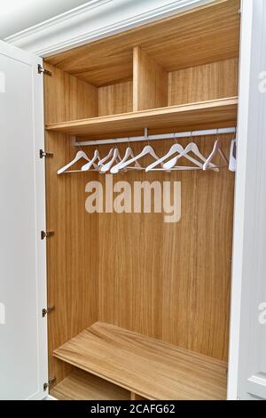 Opened white wardrobe with wooden drawers and shelves. Wooden