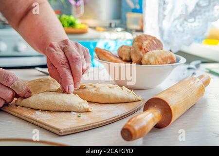 Grandma is in the kitchen baking pies. Female baker cooking bread, close up on wooden table. Baking concept, pastry products, cooking with love Stock Photo