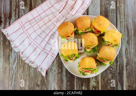 Delicious sandwiches with ham and cheese on white plate on wooden background. Stock Photo