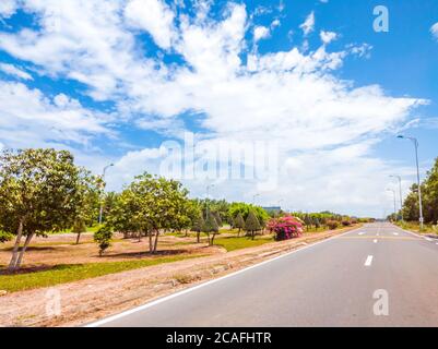 Beautiful view of wide open road with a paved highway stretching out as far as the eye can see with small green hills, pink flowers under a bright Stock Photo