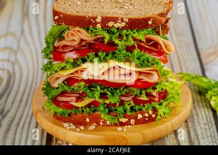 Colorful big sandwich with ham, cheese and vegetables on wooden backgrond. Stock Photo