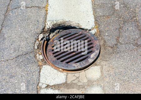 Round storm drain grate over damaged manhole on the road. Stock Photo
