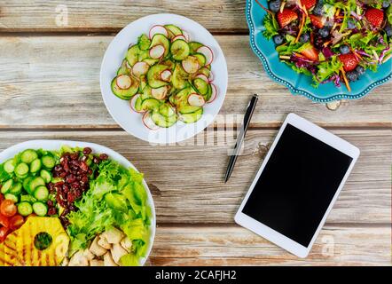 Various salads with tablet and pen on wooden table for food blogger. Stock Photo