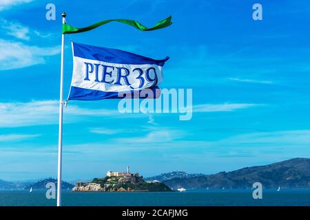 Pier 39 flag in blue sky flapping in the wind advertising a popular tourist attraction at Fisherman's Wharf. San Francisco bay coastline with famous A Stock Photo