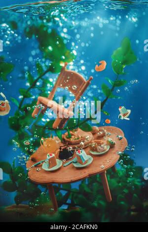 Tea party underwater, drowning table with sweets and a chair, seaweeds and bubbles, underwater still life Stock Photo