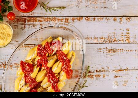 Staffed jumbo shells pasta in glass baking pan on white woodwn background. Stock Photo