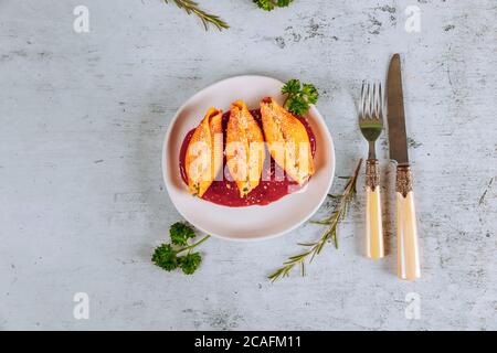 Pasta shells stuffed with ricotta, meat and parmesan on plate with tomato sauce, knife and fork. Stock Photo