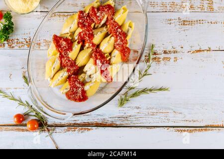 Staffed jumbo shells pasta with tomato sauce in glass baking pan on white woodwn background. Stock Photo