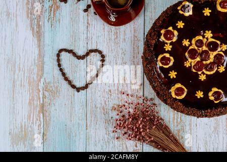Heart shape made from coffee beans with chocolate cherry cake with flowers and cup of coffee. Stock Photo
