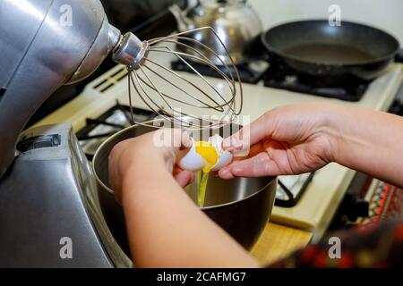 Woman separates egg white from egg yolk into mixer bowl. Stock Photo