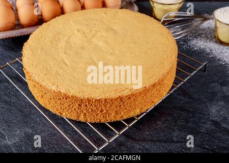 Homemade round sponge cake on gray table with eggs. Stock Photo