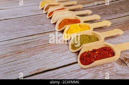 Colored ground spices powders in wooden spoons on white wooden background. Stock Photo