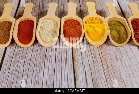Colored ground spices powders in wooden spoons on white wooden background. Stock Photo