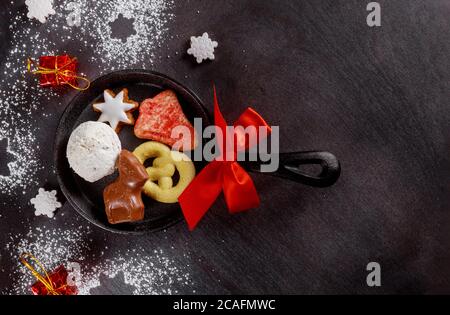 Skillet with Christmas bow, cookies and chocolate on dark table. Stock Photo