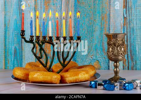 Jewish holiday Hanukkah concept. Menorah with burning candles, donuts and silver cup of wine. Stock Photo