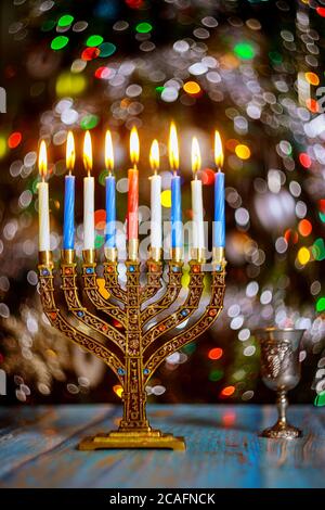 Hanukkah background with menorah and burning candles on sparkle background with defocused colored lights. Stock Photo