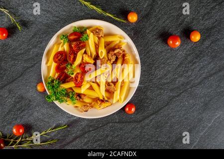 Penne pasta with halved cherry tomato and meat on black background. Stock Photo