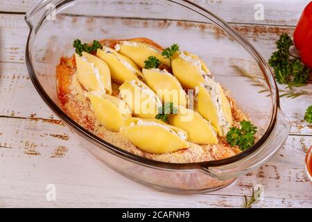 Staffed jumbo shells pasta in glass baking pan on white woodwn background. Stock Photo