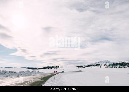 Mountain serpentine road in winter among the snow-covered plains with a view of the forest and mountains. Stock Photo