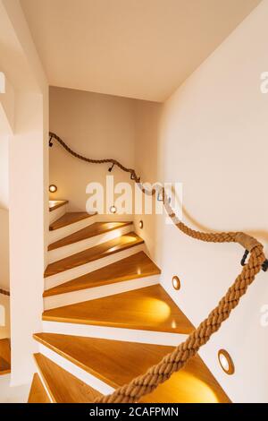 Staircase with illuminated steps and rope railings in a house with white walls. Stock Photo