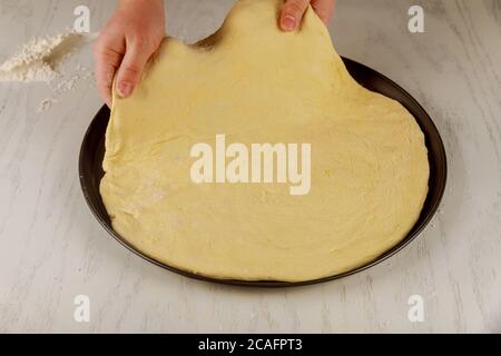 Woman puts fresh raw pizza dough on oven tray. Stock Photo