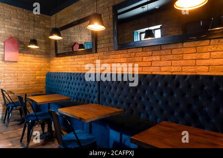 Small dining tables at restaurant, modern loft design, brick wall behind, lamps. Stock Photo