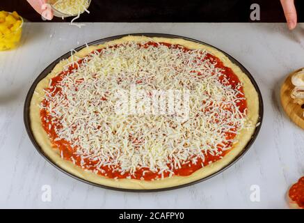 Sprinkling round pizza with shredded mozzarella cheese. Stock Photo