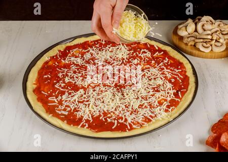 Woman sprinkling pizza with shredded mozzarella cheese. Stock Photo
