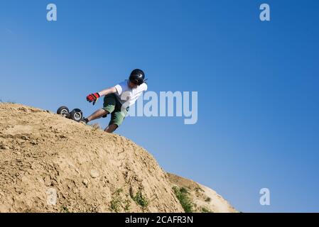 Skateboarder jumping with mountainboard over the hill with blue sky in the background Stock Photo