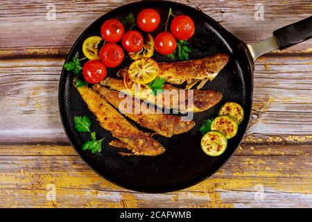 Fried whole capelin fish in a pan on a wooden background. Top view. Stock Photo