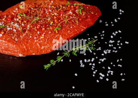 Fresh sirloin beef steak with herb, salt and peppercorn over black stone board. Stock Photo