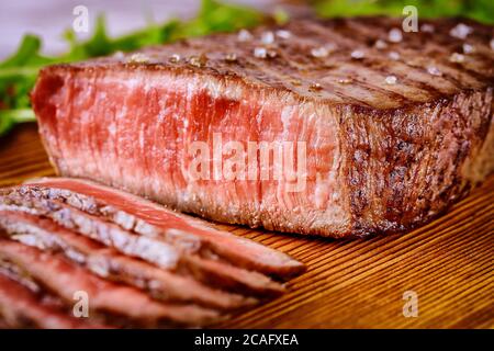 Sliced grilled rare beef steak served with arugula on wooden board. Stock Photo