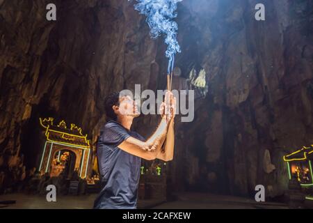 Young man praying in a Buddhist temple holding incense Huyen Khong Cave with shrines, Marble mountains, Vietnam Stock Photo