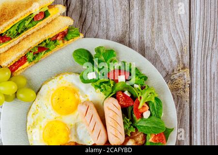 Pork franks, fried eggs, grilled cheese sandwiches and salad for breakfast. Stock Photo