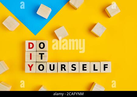 DIY and do it yourself words written on wooden blocks on yellow background. Flat lay view. Stock Photo