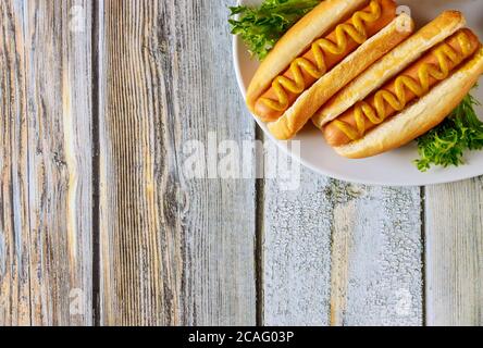 Hot dog with mustard on white plate on wooden background. Stock Photo