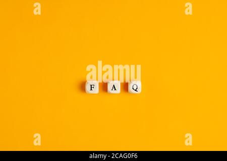 FAQ Frequently asked questions text written on wooden blocks on yellow background. Service support or assitance concept. Stock Photo