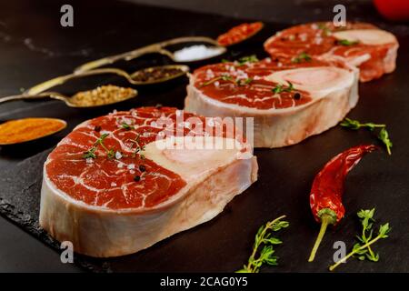 Fresh cut beef shank in bone and seasonings in spoons on black board. Stock Photo