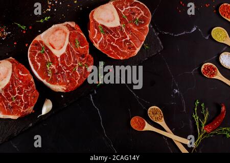 Fresh cut beef shank in bone and seasonings in spoons on black board. Stock Photo
